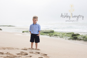 boy poses in front of green rocks on beach