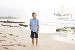boy poses on beach with blue shirt