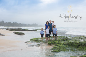 family poses on green rock at the beach