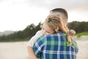 dad holds daughter with flower on beach