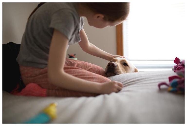 little girl sits on bed with dog