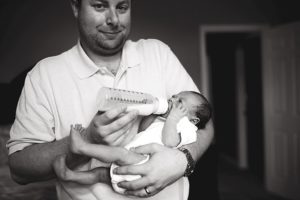 dad feeding newborn baby with a smirk on his face
