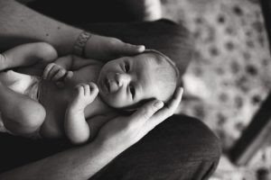 black and white photo of baby laying in dads hands