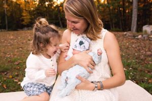 mom toddler girl and newborn baby boy sitting together with an autumn backdrop