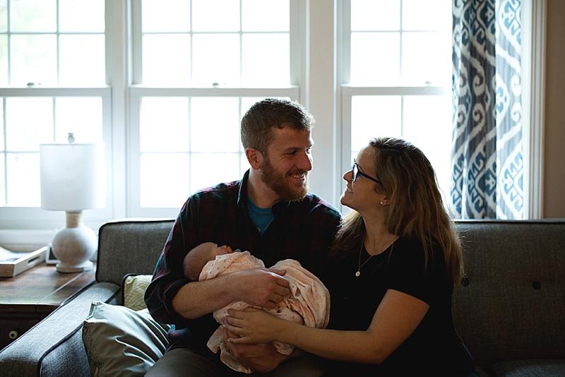couple sit on couch with newborn baby