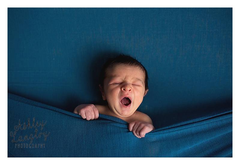 baby yawns on blue backdrop