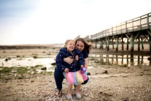 mom tickles daughter on the beach