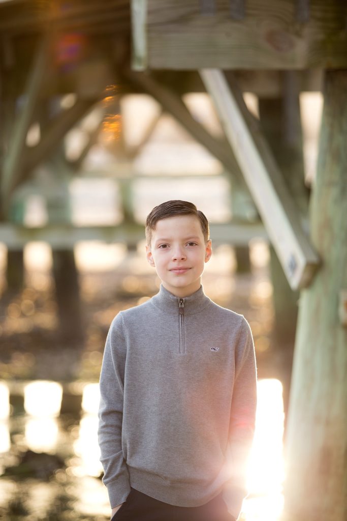 young boy poses under pier