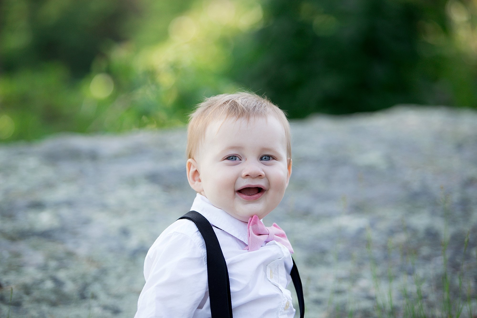 tiny boy in boy tie sits on a rock