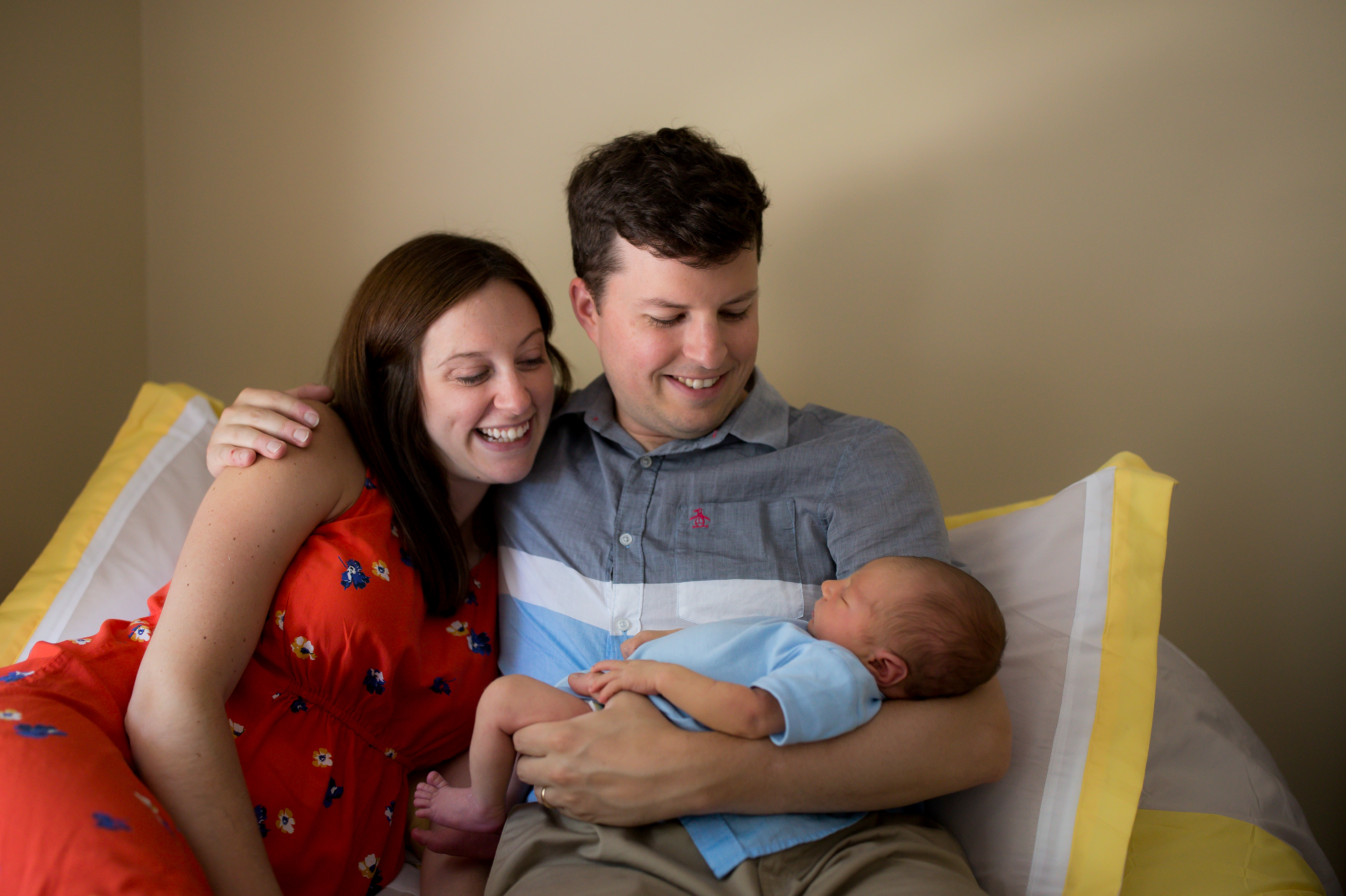mom and dad snuggle newborn baby in bed