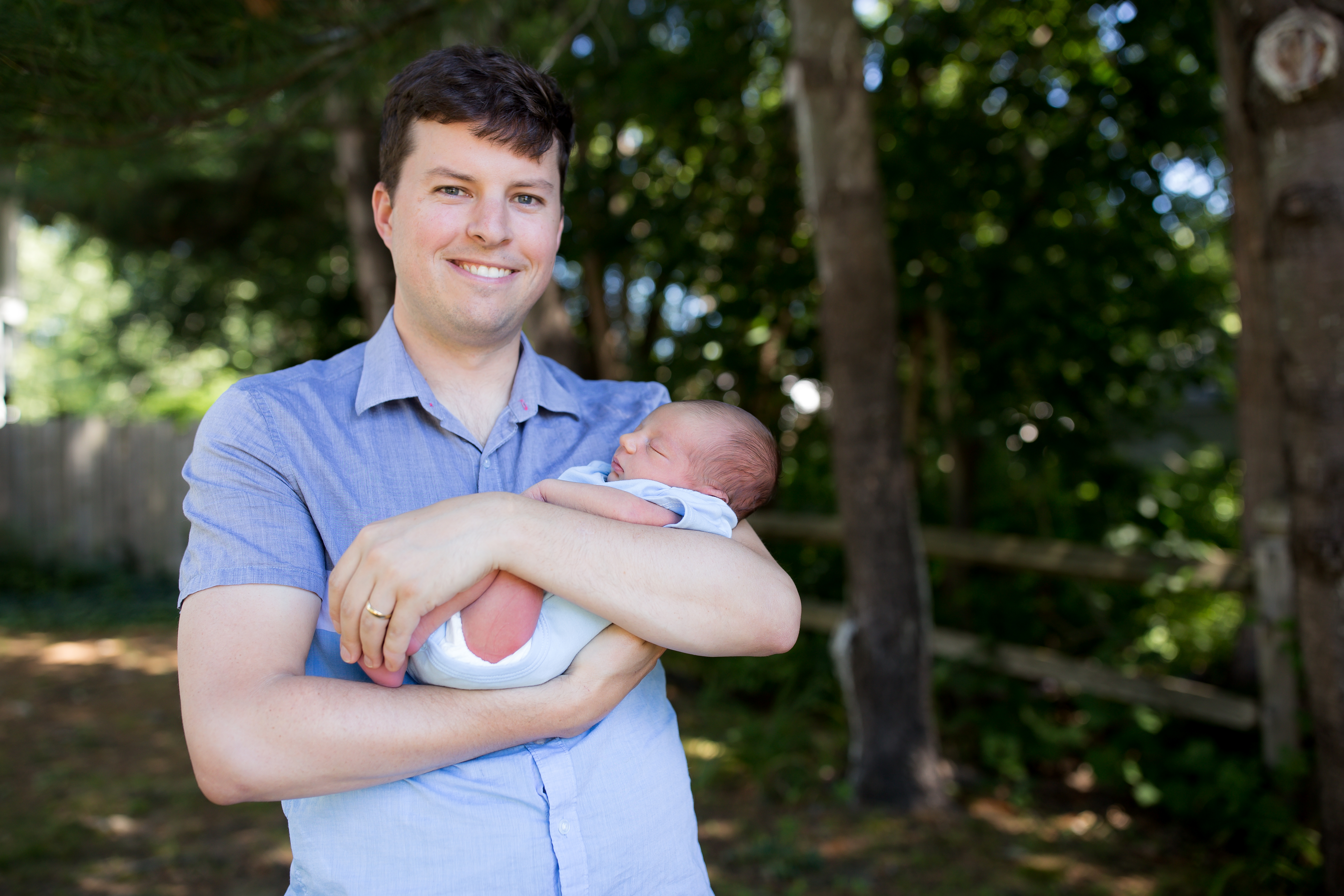 dad holds newborn son under tree