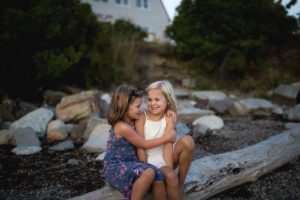 sisters hug on driftwood in harpswell maine