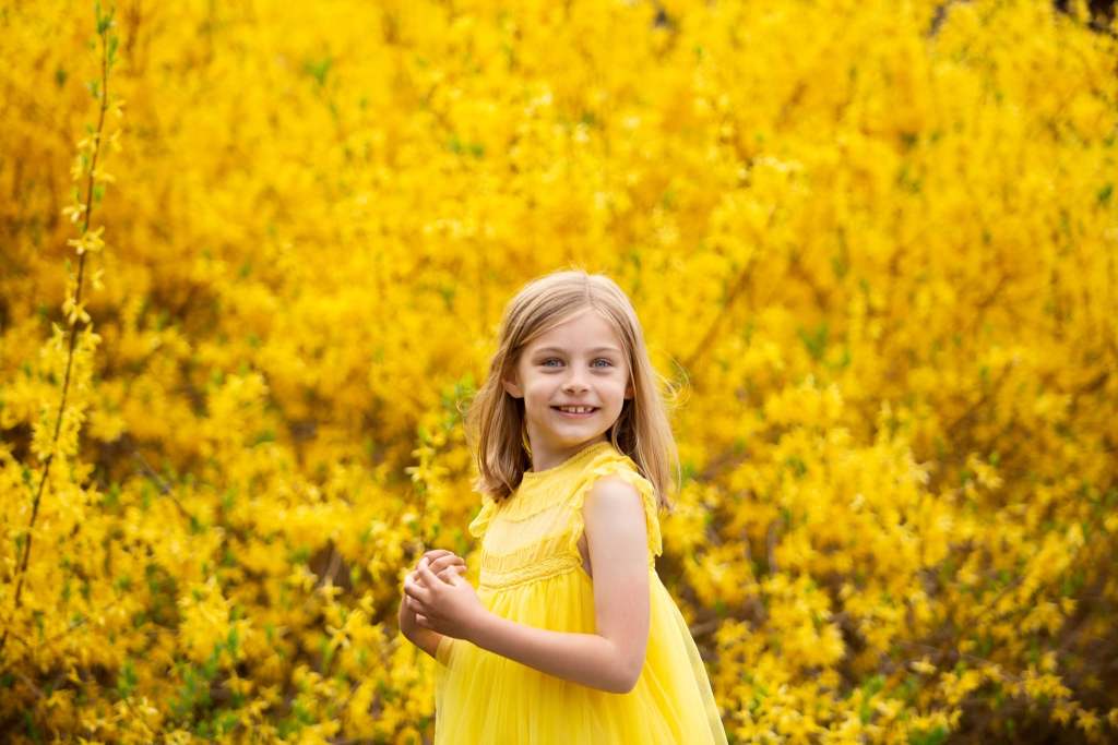 girl in yellow dress in front of yellow flowers